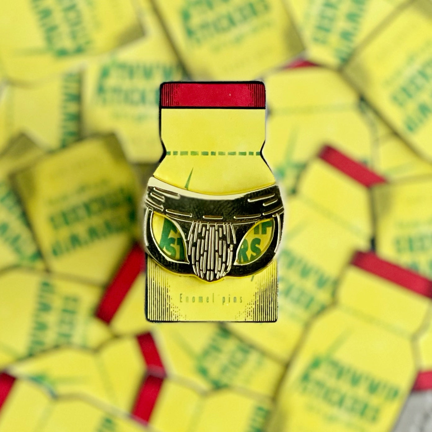 Image of a golden jockstrap mini pin on a poppers themed backing card